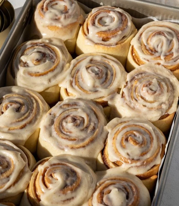 Freshly baked cinnamon rolls drizzled with icing on a wooden table