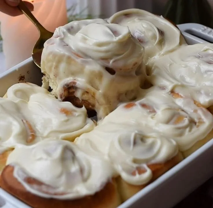 Freshly baked, fluffy cinnamon rolls drizzled with creamy icing on a wooden table.
