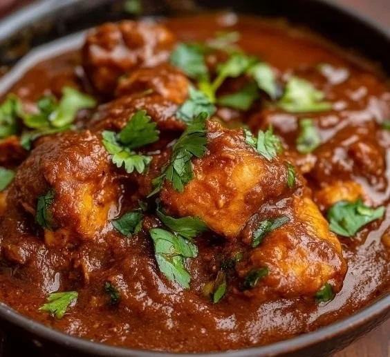 A vibrant plate of Rogan Josh chicken topped with fresh herbs and spices.