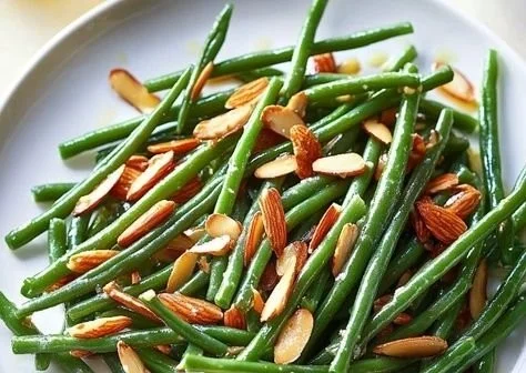 Sautéed green beans with garlic and almonds in a serving dish.