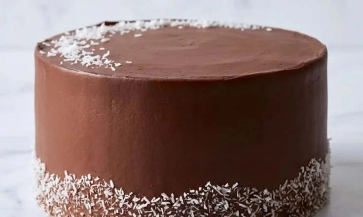 A slice of moist Chocolate Coconut Cake topped with shredded coconut and chocolate frosting.